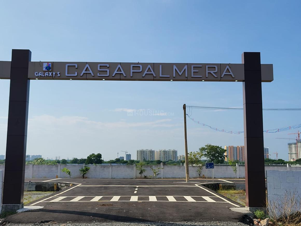 1000015554 The main entrance gate of "Galaxy's CASAPALMERA," featuring a dark brown archway with illuminated letters, a newly paved road, and distant residential buildings under a clear sky.